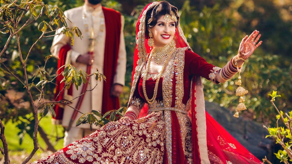 South Asian bride in red and gold bridal lehenga with groom in sherwani